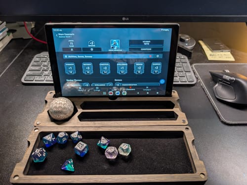 Reviewer's large, matte silver Orb D100 metal die resting in a wooden holder on a desk.