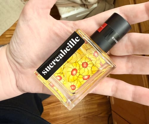 Customer holding a square glass bottle of Cherry Almond Cookie perfume in their hand, showing the yellow cookie-themed label.
