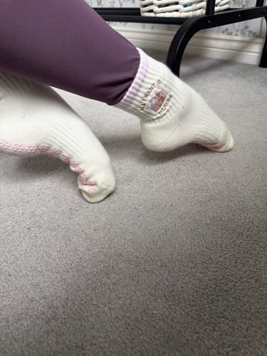 Reviewer wearing the white 'All I Want Is Pilates' socks, showing the logo and pink grips.