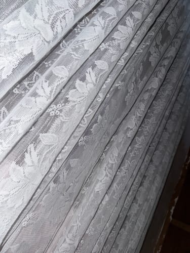 Customer's photo of a draped, white lace curtain with a floral pattern.