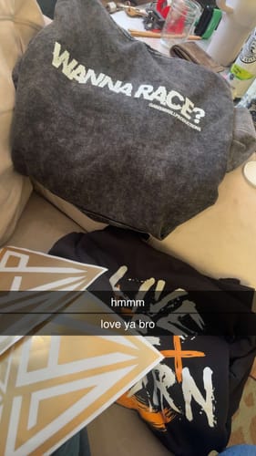 Reviewer's photo of a grey hoodie with 'WANNA RACE?' print, alongside other shirts and stickers.