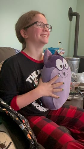A reviewer smiling happily while holding the purple Derek Squishy Plush in their lap.