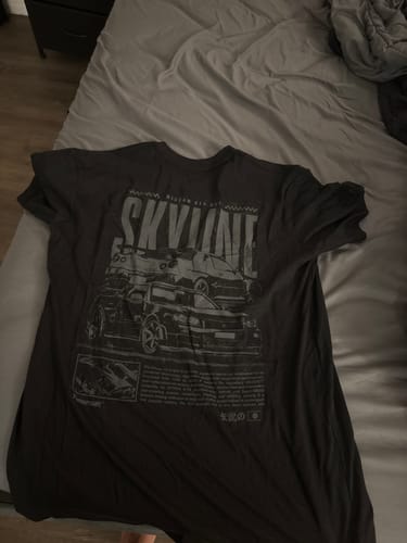 Customer's dark TOKYO TRIBUNE TEE with a large car graphic print laid flat on a bed.