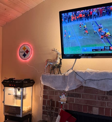 Customer's Steelers Steelmark wall art with red backlighting mounted in a living room next to a TV showing a game.
