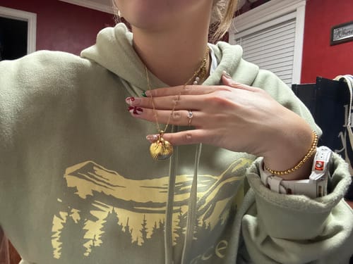 A reviewer wearing the Destin Necklace with its gold shell-shaped pendant against their chest.