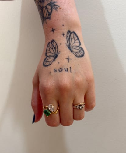 Reviewer's hand showing the Navae Birthstone Ring with its green and clear stones.