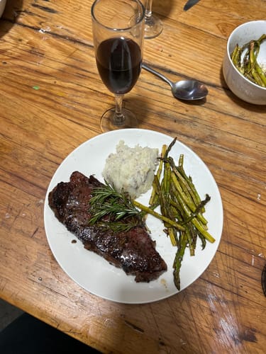 Cliente mostrando su New York Steak Choice servido en un plato con espárragos y puré.
