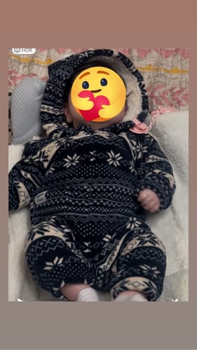 عميل يعرض طفلاً يرتدي سالوبيت إجازات سعيدة المنقوش وهو مستلقٍ.