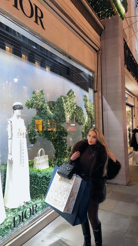 Reviewer wearing the dark Faux Mink Pelted Coat while posing outside at night with shopping bags.