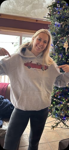 Reviewer smiling and pointing to their oversized drop top grey hoodie, showing the front graphic and fit with leggings.