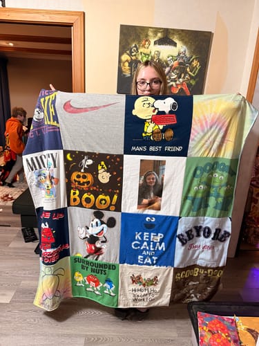 Customer peeking over their large Premium T Shirt Quilt made from various colorful t-shirts.