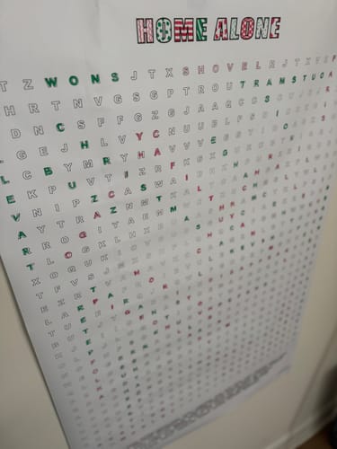 Close-up of a reviewer's Home Alone Giant Word Search Puzzle hanging on a wall, showing the festive letters.