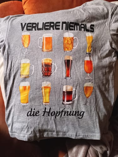 Kunde zeigt das graue Premium-Shirt mit dem Aufdruck „Verliere niemals die Hoffnung“ und vielen Biergläsern.