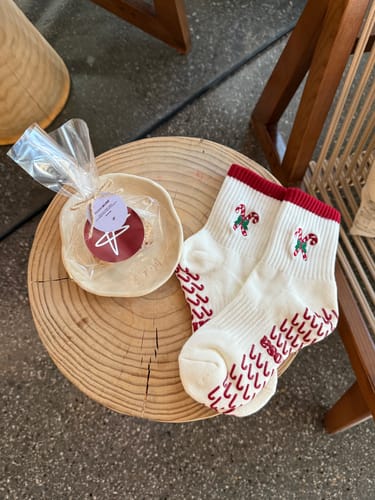 Customer's off-white Candy Christmas socks with a red trim and candy cane design, laid on a wooden surface.