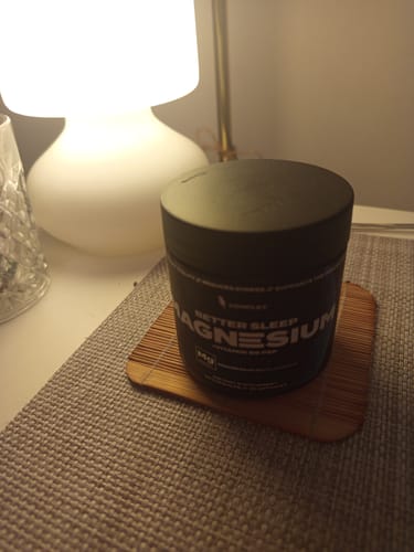Customer's tub of Complex Sleep Magnesium resting on a bedside table next to a lamp.