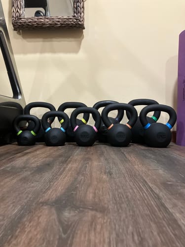 Customer's set of black Strength Shop Cast Iron Kettlebells with colored handle markings, lined up on a wood floor.