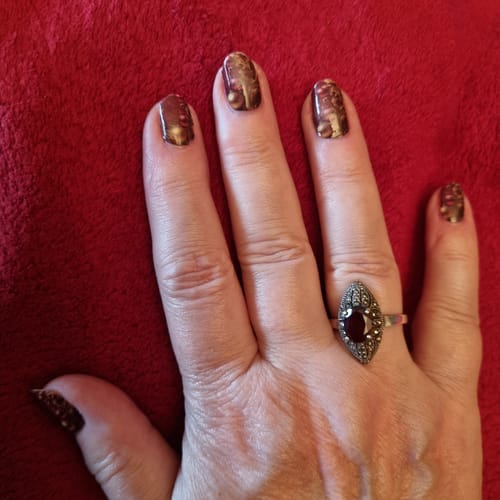 Nahaufnahme der Hand einer Kundin, die die burgunderroten Scarlet Holiday Nagelfolien mit goldenen Akzenten trägt.