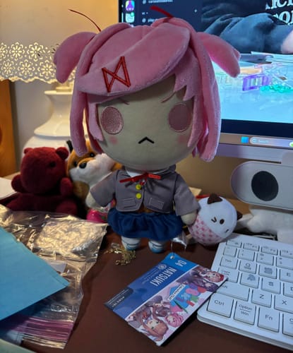 Customer's Natsuki Collector's Plush standing on a messy desk with its collector's card and cupcake accessory.