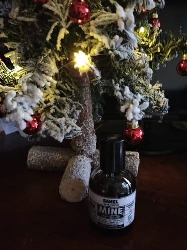 Recensore mostra il flacone di profumo SAHEL davanti a un albero di Natale.