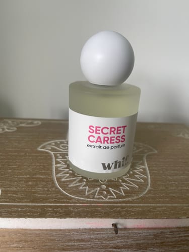 Customer's Secret Caress perfume bottle with a round white cap, sitting on a carved wooden surface.