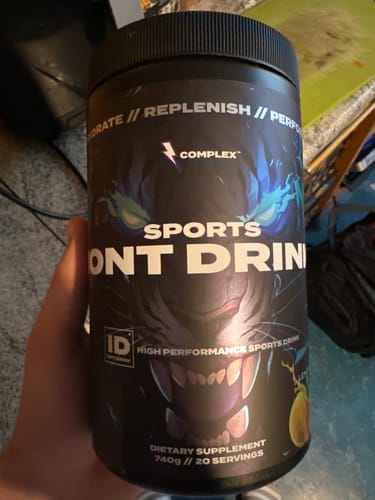 Reviewer holding the black tub of Complex Iont Drink, displaying its bold graphic label.