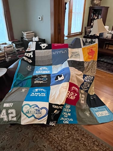 Customer's custom Premium T Shirt Quilt, a colorful patchwork of memorable shirts, draped over a sofa in a living room.