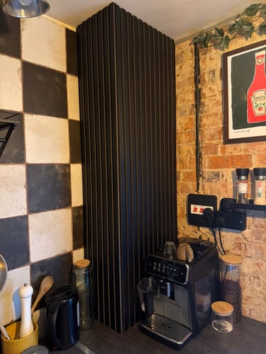 Reviewer's two black acoustic slatted wall panels installed in a kitchen corner next to a coffee machine.