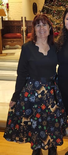 Reviewer wearing the black Christmas print dress with a full skirt in front of a decorated Christmas tree.