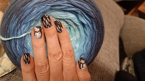 Hand einer Kundin, die die 'A Frosty Visit' Nagelfolien mit einem niedlichen Schneemann- und Tannenmotiv auf den Nägeln trägt.