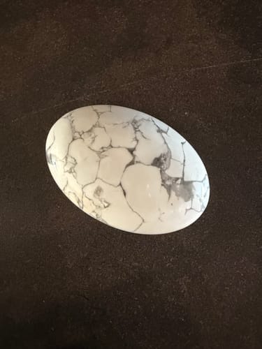 Photo d'un client montrant son galet d'Howlite blanc avec des veines grises sur une surface sombre.