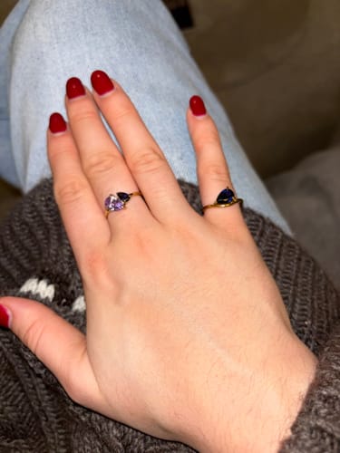 Customer's hand wearing the gold Pia Birthstone Ring with a blue stone on the pinky, shown with another ring.