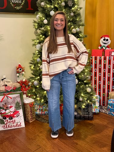 Reviewer wearing the Ribbed Multi Striped Sweater with wide-leg blue jeans in a festive setting.