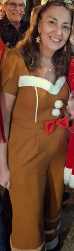 Reviewer smiling at an event while wearing the brown gingerbread jumpsuit with its white icing trim and red bow.