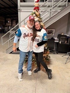 Two customers wearing their matching white and blue custom jerseys in front of a Christmas tree.