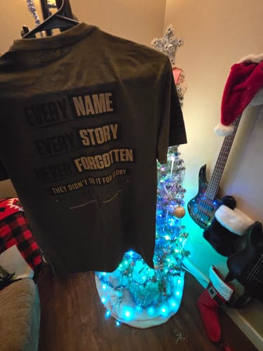 Customer showing the back of a dark T.V.P. Elite Membership t-shirt with text reading "Every Name Every Story Never Forgotten".