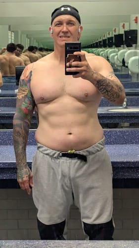 Reviewer with multiple large tattoos on their arms taking a shirtless mirror selfie in a locker room.