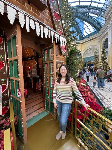 Reviewer wearing the Cascading Colors Striped Sweater with blue jeans while standing in a festive conservatory.