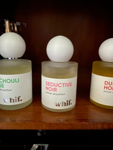 Customer's Seductive Noir perfume bottle, centered between two other scents on a wooden shelf.