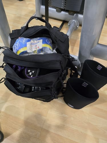 Customer's open black Training Backpack 2.0 on a gym floor, showing its spacious interior filled with workout gear.