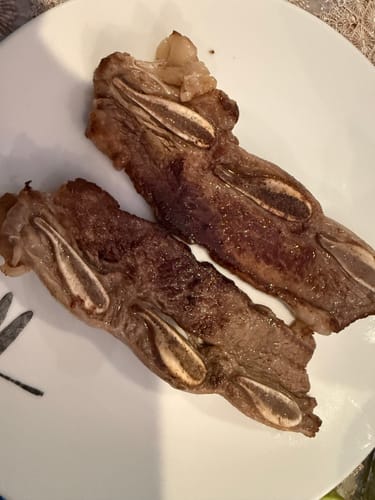 Cliente mostrando dos tiras de asado de tira ya cocinadas en un plato blanco.