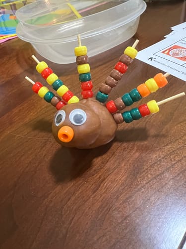 Customer's turkey craft from The Preschool Box, made with brown playdough and colorful beads for feathers on a wood table.