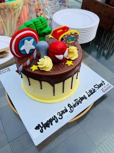 Customer's vibrant Superhero Drip Cake with detailed fondant superhero symbols over a chocolate-drizzled base.