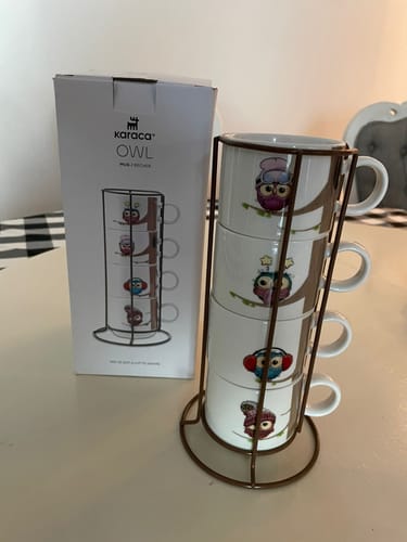 Customer's Karaca Owl mugs stacked in their metal stand, with the product packaging shown alongside on a table.