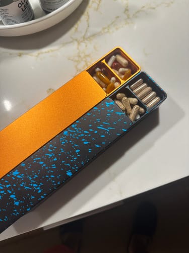 Customer's two open Weekly AM-PM Vitamin XL Cases, one orange and one black with blue splatters, filled with vitamins.