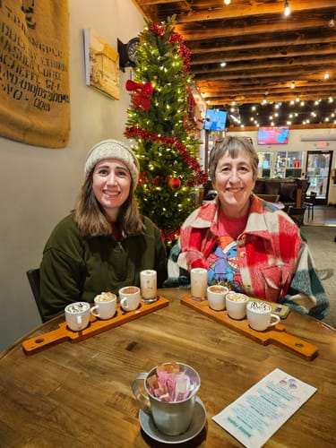 Reviewer wearing the Red and Green Plaid Shacket while sitting at a table next to a Christmas tree.