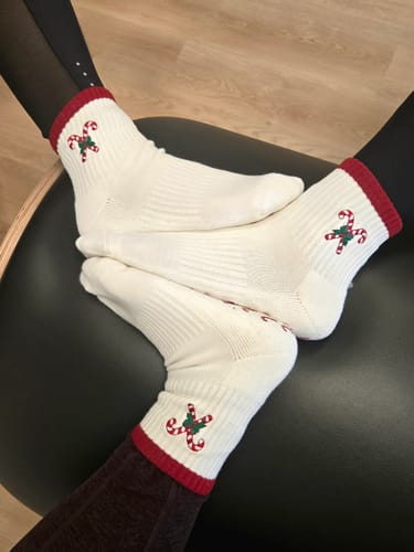 Three reviewers show off their matching white Candy Christmas socks with a red cuff and candy cane embroidery.