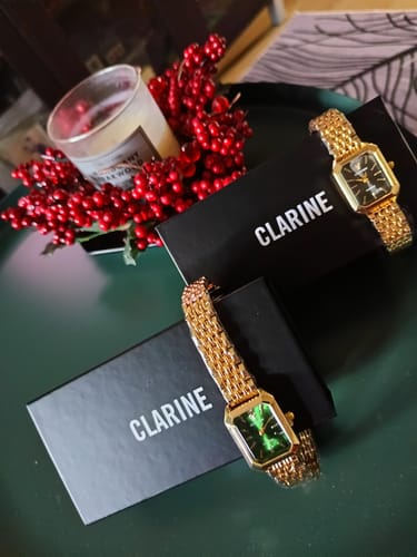 Reviewer's two gold CLAIRE DE MAINS watches, one with a green face and one with a black face, displayed on a dark tray with packaging.