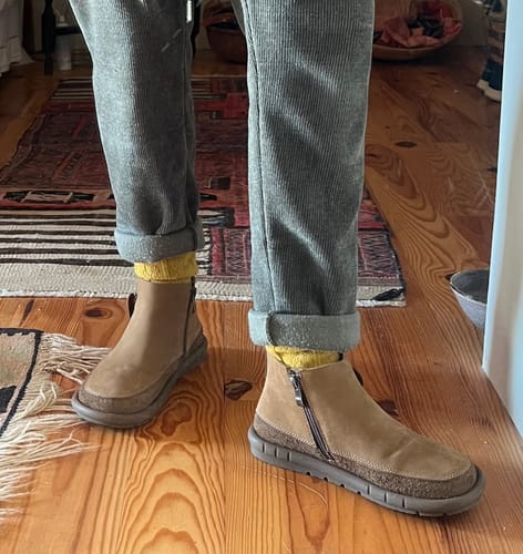 Reviewer showing the fit of the brown vintage leather boots with rolled grey pants and yellow socks.