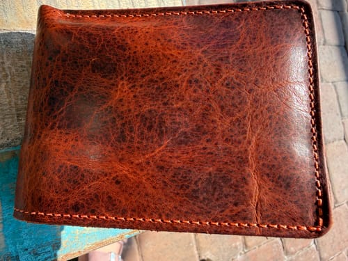 A reviewer's Lanier Premium Bison Bifold wallet, showing the rugged, textured brown leather and detailed stitching.