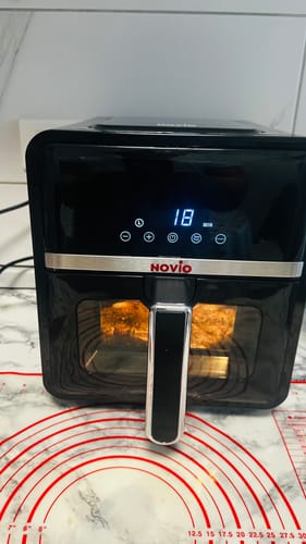 Un client arată friteuza Air Fryer Novio StonePro în timpul utilizării. Ecranul digital este aprins și arată 18 minute.